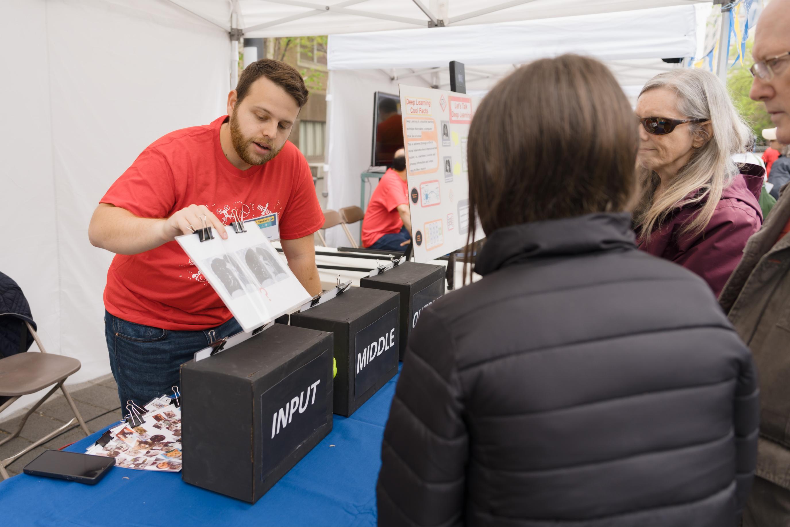 A volunteer showing photos of lung X-rays to three participants at the Deep Learning Booth.